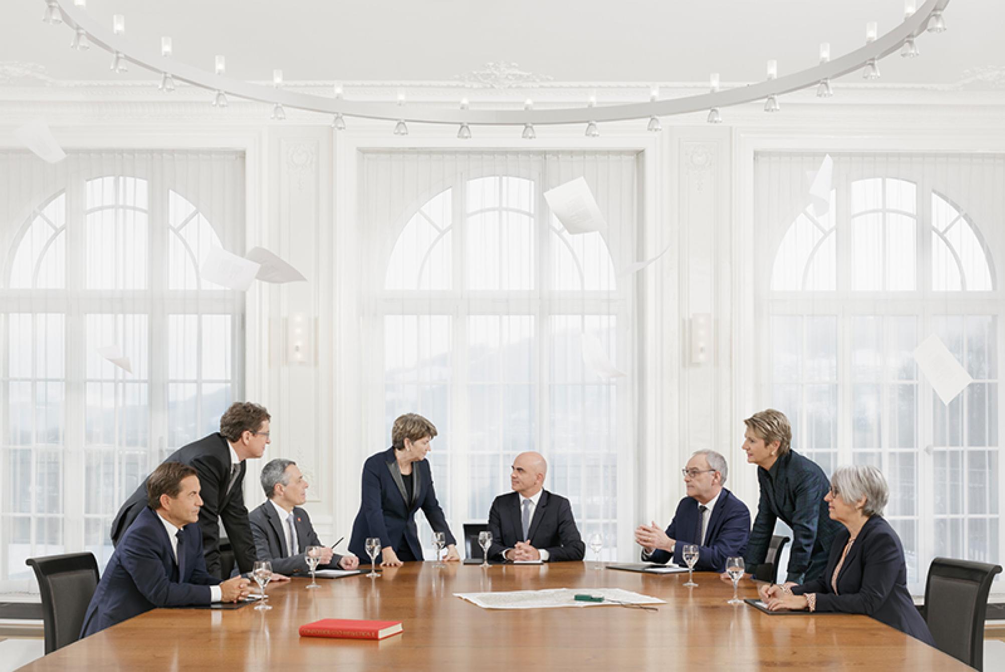 Das Bild zeigt das offizielle Bundesratsfoto 2023 mit den sieben Mitgliedern des Bundesrats und dem Bundeskanzler. Sie sitzen alle an einem runden Tisch und sprechen miteinander.