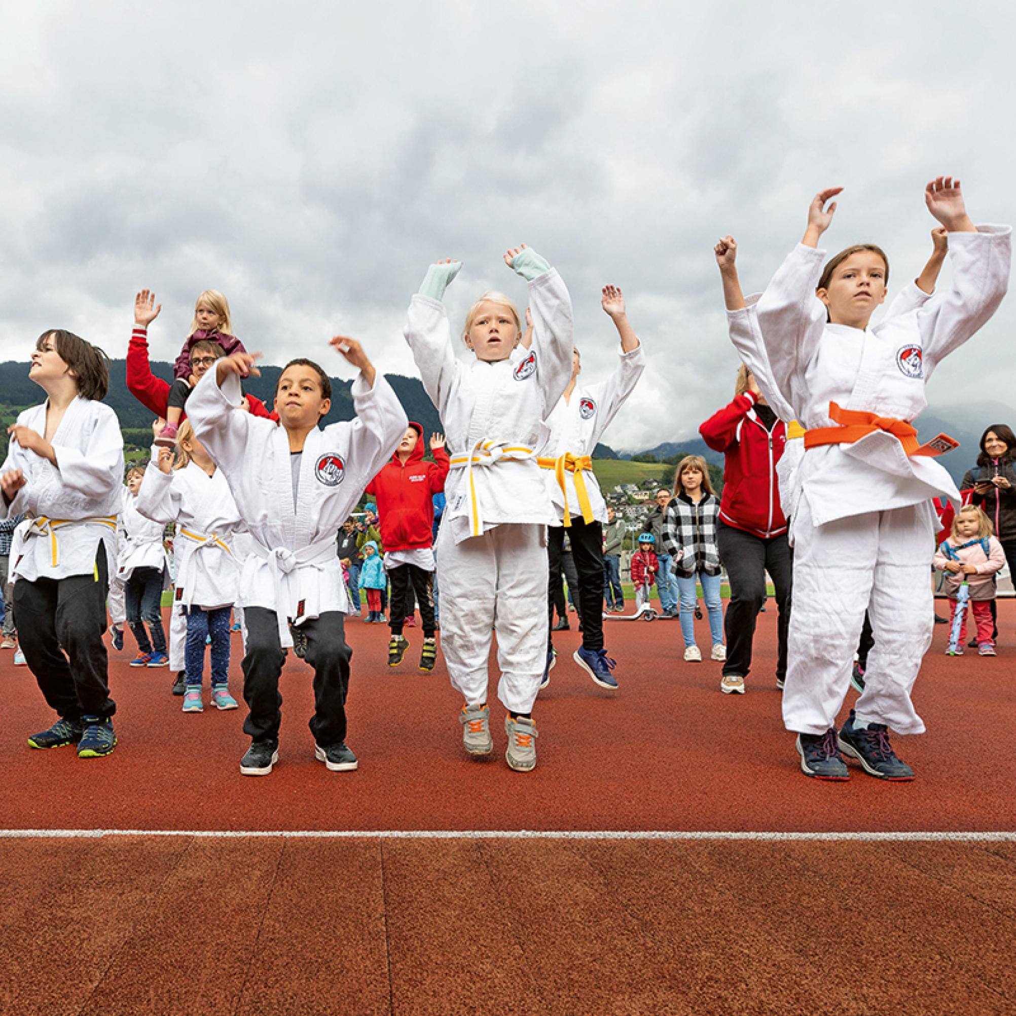 The photo shows a group of children in judo attire. They all jump in the air simultaneously.