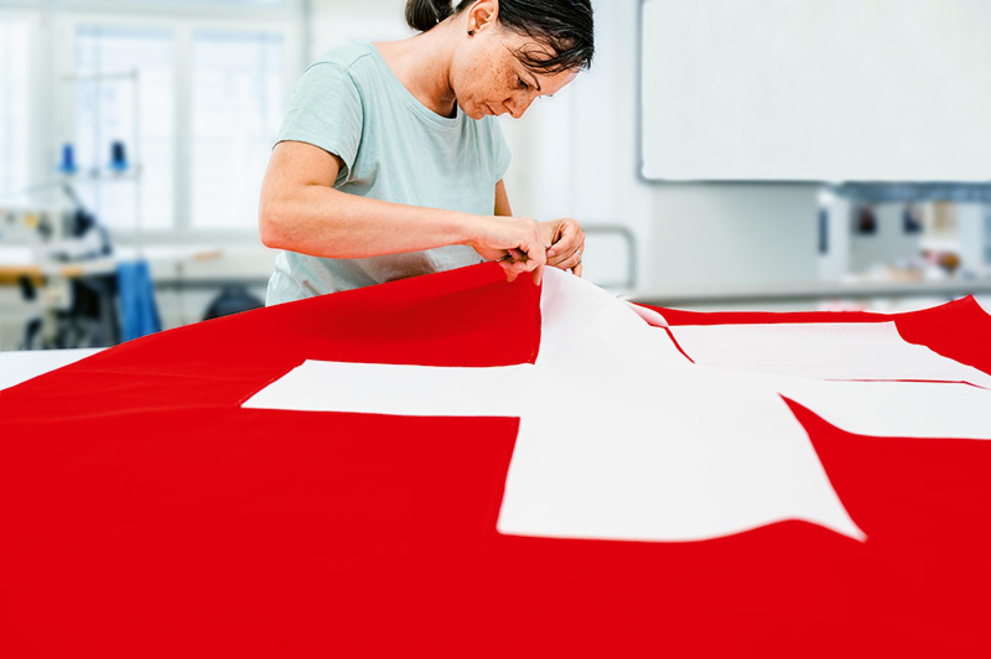Das Bild zeigt eine Frau, die in einem Atelier eine grosse Schweizer Fahne näht.